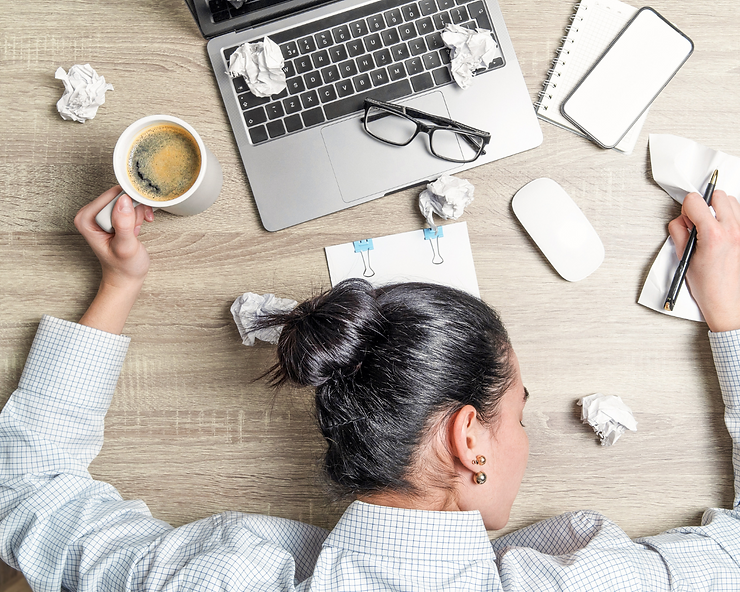 Mujer con la cabeza en un escritorio de oficina durmiendo con una taza de café en la mano